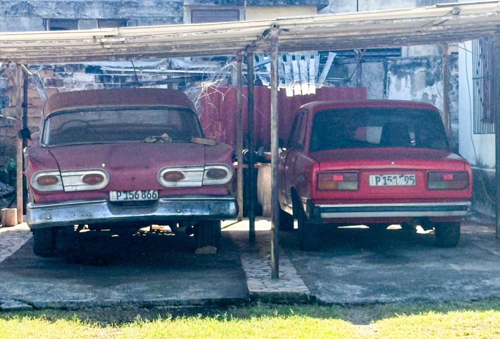 An old American car and a Russian Lada, parked in a side yard. Not fancy, just everyday Cuban cars.